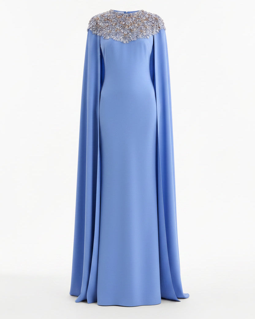 A floor-length light blue gown with a draped cape-like silhouette and a heavily embellished silver beaded yoke, shown on a plain white background.